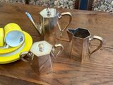 a wooden table with a yellow plate and a silver coffee pot and a yellow plate and a silver tea pot and a yellow plate and a silver cup