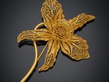 une broche en forme de fleur plaquée or, ornée de feuilles, sur fond noir