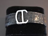 black leather cuff bracelet with a silver d buckle on a black velvet cuff