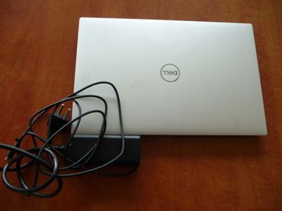 dell laptop with charger and cable plugged to it on a wooden table