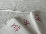 trois serviettes blanches ornées de motifs brodés rouges, posées sur une table