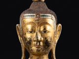 une tête de Bouddha dorée posée sur un socle, sur fond noir