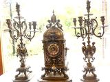 trois bougies et une horloge posées sur une table devant une fenêtre