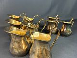 six antique brass pitchers with handles and handles on a grey background