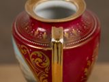 a red and gold vase with a gold handle on a table