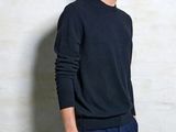 the man is standing in front of a white wall wearing a black sweater and blue pants