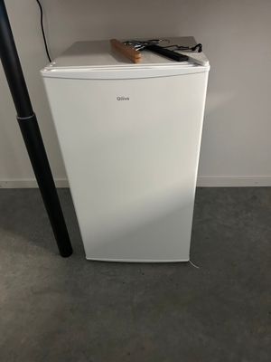 a small white refrigerator with a remote control on top of it
