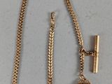 une photo d'un collier en or orné d'une breloque en forme de clochette et d'une chaîne