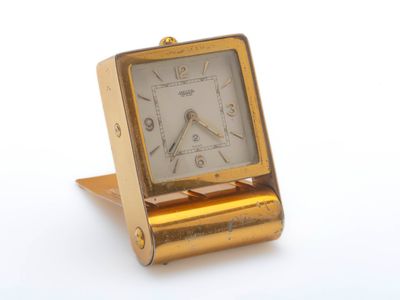 une petite horloge dorée posée sur un socle, sur une surface blanche