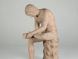 statue of a man sitting on a rock with his hands on his knees