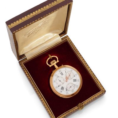 une montre de poche en or dans un écrin rouge posé sur une surface blanche
