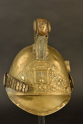 un casque doré ancien posé sur un socle, sur fond noir