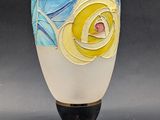 a white vase with a yellow rose on it on a wooden stand