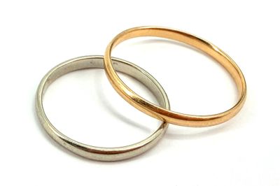 two gold and silver wedding rings on a white surface