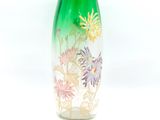 a green vase with flowers on it on a white surface