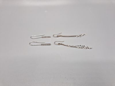 Deux paires de boucles d'oreilles en argent sont posées sur une surface blanche.