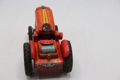 un petit tracteur rouge avec un volant, posé sur une surface blanche