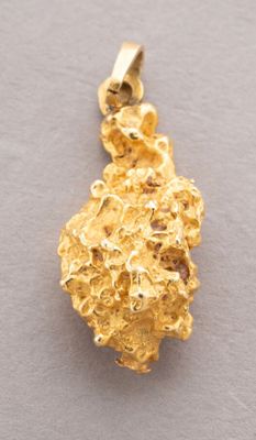 a close up of a gold nugget pendant on a gray surface