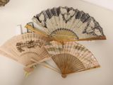Plusieurs anciens ventilateurs sont exposés sur un fond blanc, avec un miroir en arrière-plan.