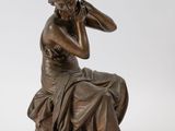 a bronze statue of a woman sitting on a rock with her hand on her head