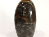 une image représentant un vase en pierre marron et noir posé sur une surface blanche