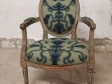une vieille chaise dont l'assise est recouverte d'un tissu bleu et vert