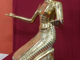 statue d'une femme vêtue d'une robe dorée, assise sur un socle en bois