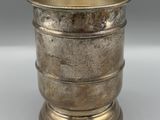 une coupe ancienne en métal argenté, posée sur un socle, sur une surface blanche