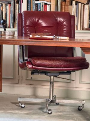 a desk with a chair and bookshelf in the background