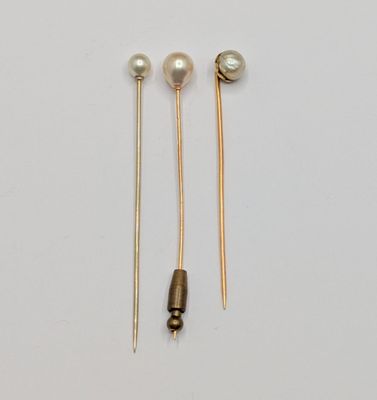 two pairs of gold and pearl ear pins on a white surface