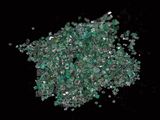 green crystals are scattered in a pile on a black surface