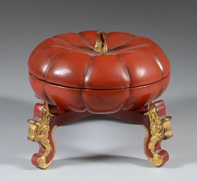 une boîte rouge et dorée en forme de citrouille posée sur un socle