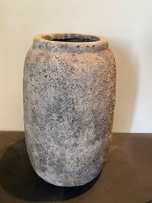 un vase en pierre posé sur une table, avec un mur blanc en arrière-plan