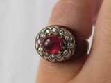 an image of a woman ' s hand holding a ring with a red stone