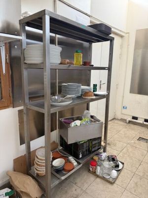 une étagère en acier inoxydable sur laquelle sont posés de la vaisselle et des casseroles, dans une cuisine