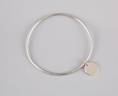 a silver bang bracelet with a disc charm on it