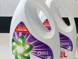 trois flacons de lessive Ariel posés sur un plan de travail, à côté d'une tasse de café