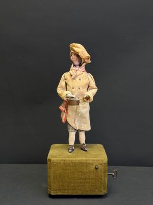 figurine représentant un homme vêtu d'un manteau jaune et d'un chapeau, debout sur une valise
