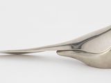 figurine d'oiseau en argent posée sur une surface blanche, avec un fond blanc