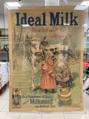 une affiche sur laquelle on peut lire « lait idéal » et qui représente une femme en train de traire une vache
