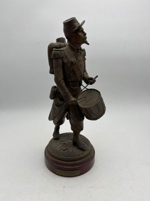 statue d'un homme portant un tambour et un chapeau, posée sur une surface blanche