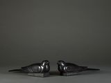 two black birds are sitting on top of each other on a gray surface
