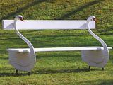 a white bench with two swans on it in the grass