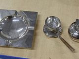 un cendrier en argent, une cuillère et un repose-cuillère posés sur une table