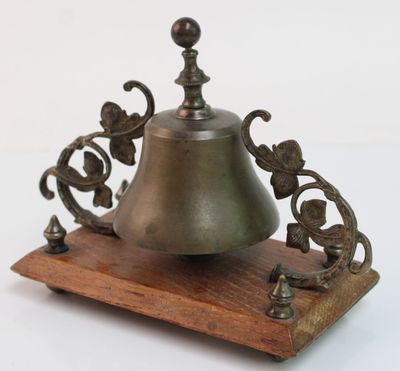 une petite cloche posée sur un socle en bois, sur fond blanc