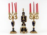 three black and gold candelabs with red candles on them