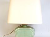a green table lamp with a white shade on top of it