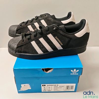une paire de baskets Adidas noires et blanches dans une boîte bleue