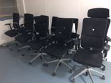 Plusieurs chaises de bureau noires sont alignées en rang dans une pièce