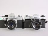 two cameras sitting next to each other on a white surface